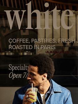 Man in a denim jacket drinking a cold beverage outside WHITE Coffee, a specialty coffee shop in Paris known for fresh roasts.