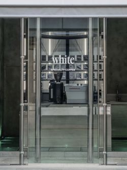 Entrance of WHITE Coffee specialty coffee shop with modern glass doors and visible coffee equipment inside.