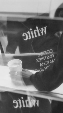 Main tenant une tasse de café devant une vitre avec le logo et menu de White Coffee à Paris 9.