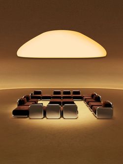 Modern seating arrangement with brown cushioned chairs and sofas under a large warm ceiling light in a coffee shop setting.