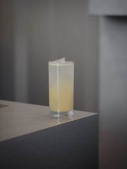 Verre de boisson jaune pâle avec glaçons posé sur un comptoir gris dans un café.