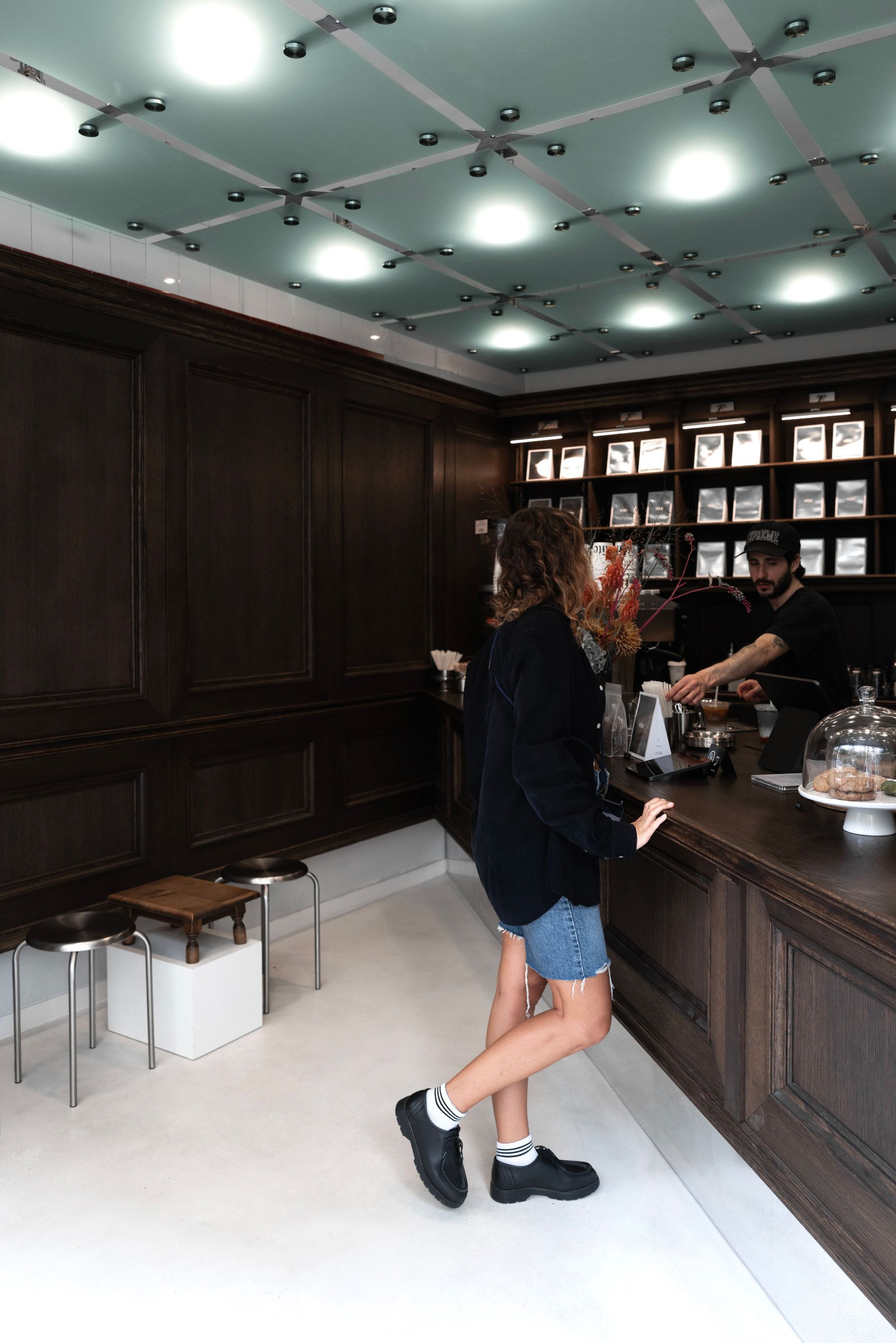 Intérieur d'un coffee shop avec comptoir en bois, barista préparant un café pour une cliente.