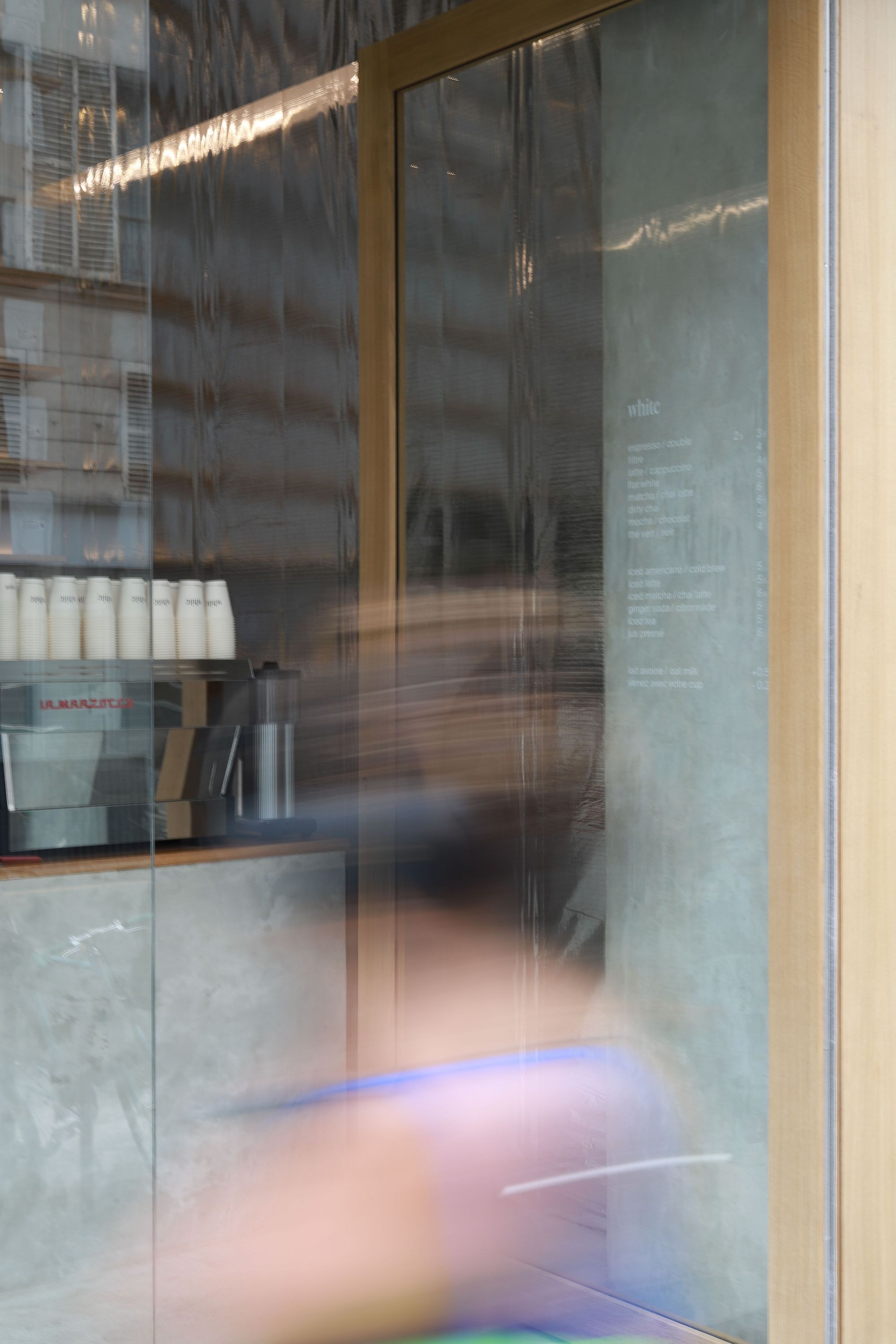 A coffee shop entrance showcasing sleek design, featuring a menu and coffee equipment in the background.