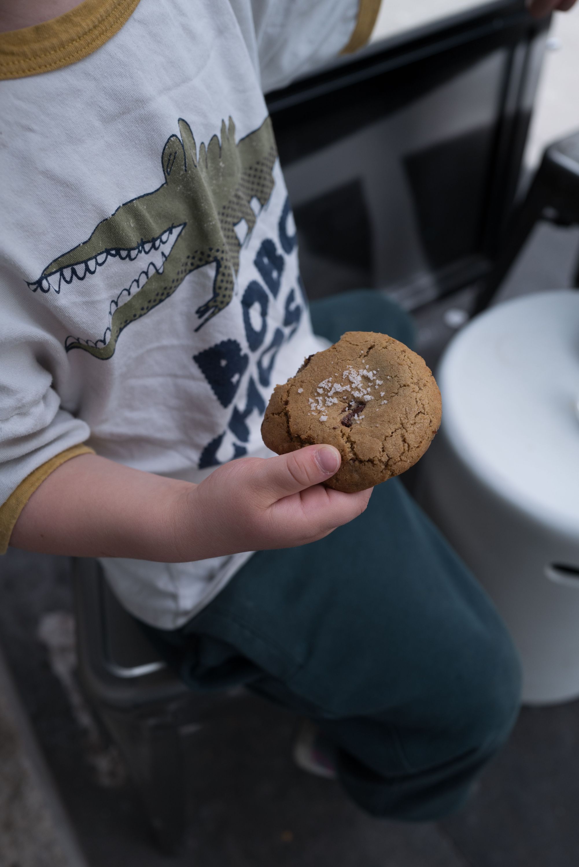 Un enfant tient un cookie aux pépites de chocolat près d'un café.