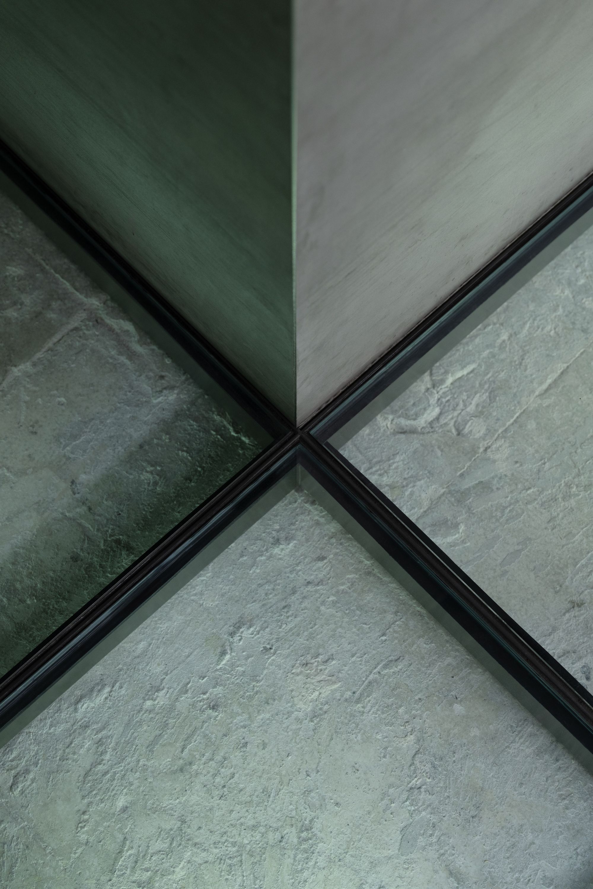 Close-up of a textured stone floor reflected in a window with black frames, creating a symmetrical pattern.