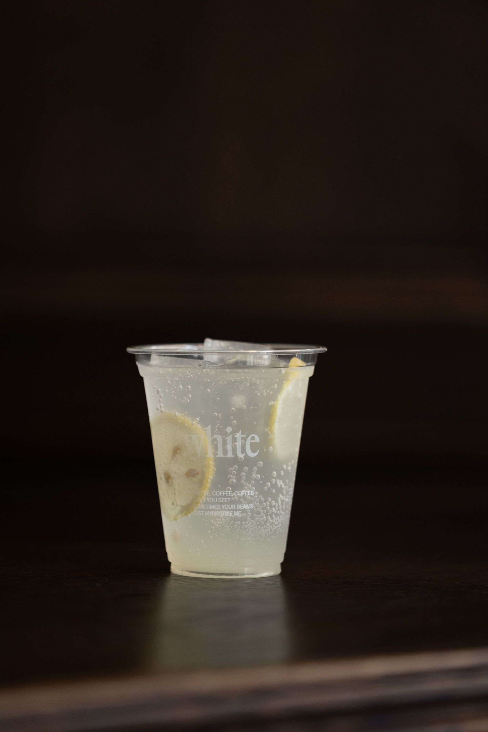 Clear plastic cup with sparkling lemon water on a dark surface at WHITE Coffee - Paris 9